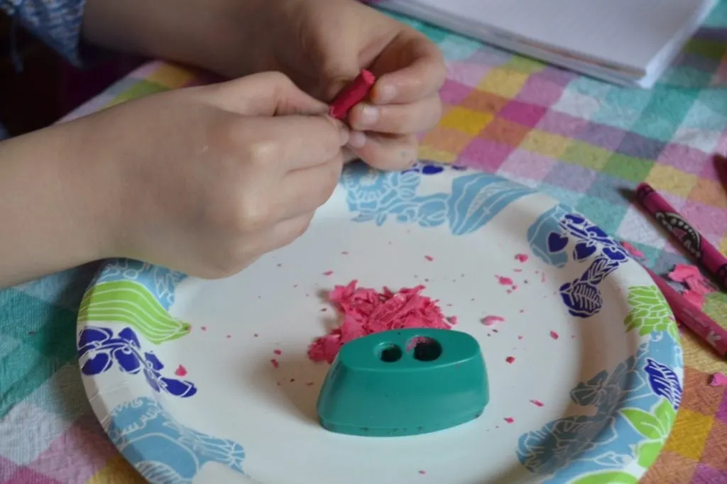 A picture of a kid sharpening crayons with a teal crayon sharpener.