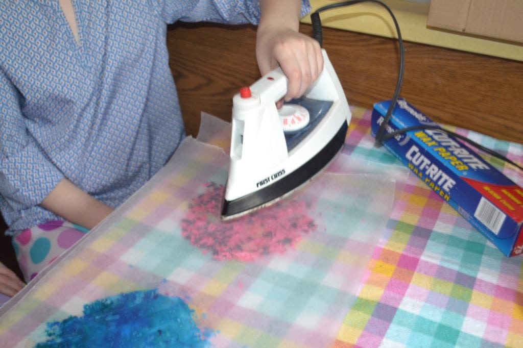 A picture of a kid ironing crayon shavings between pieces of wax paper to make a sun catcher.