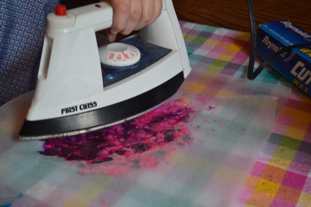 A picture of a kid ironing pink and purple crayon shavings to make a sun catcher.