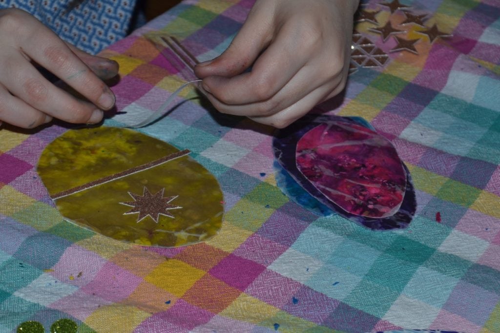 A picture of an egg shaped melted crayon sun catcher being decorated with stickers.