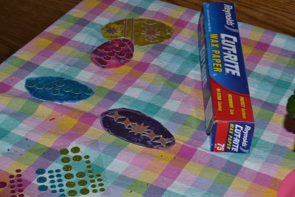 A picture of a purple and blue egg crayon shaving sun catchers with sticker decorations.
