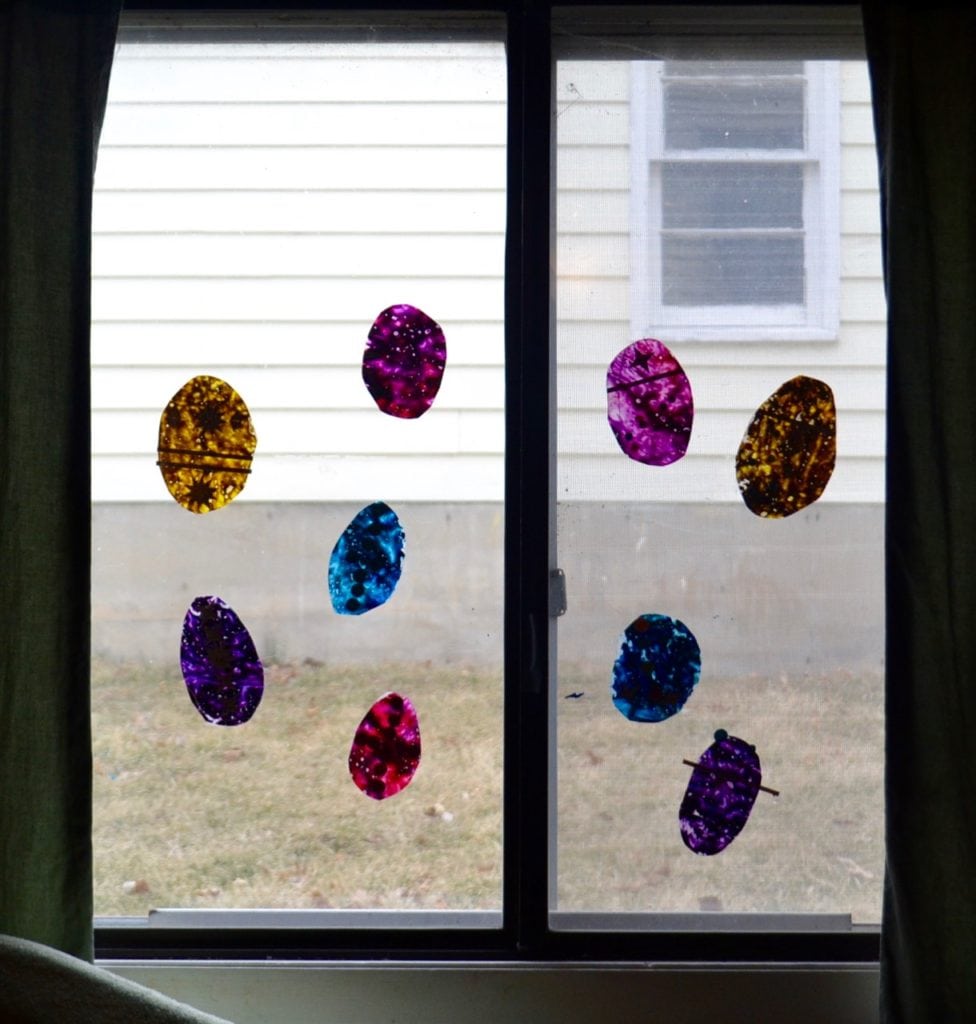 A picture of a window filled with egg shaped sun catchers made from crayon shavings.
