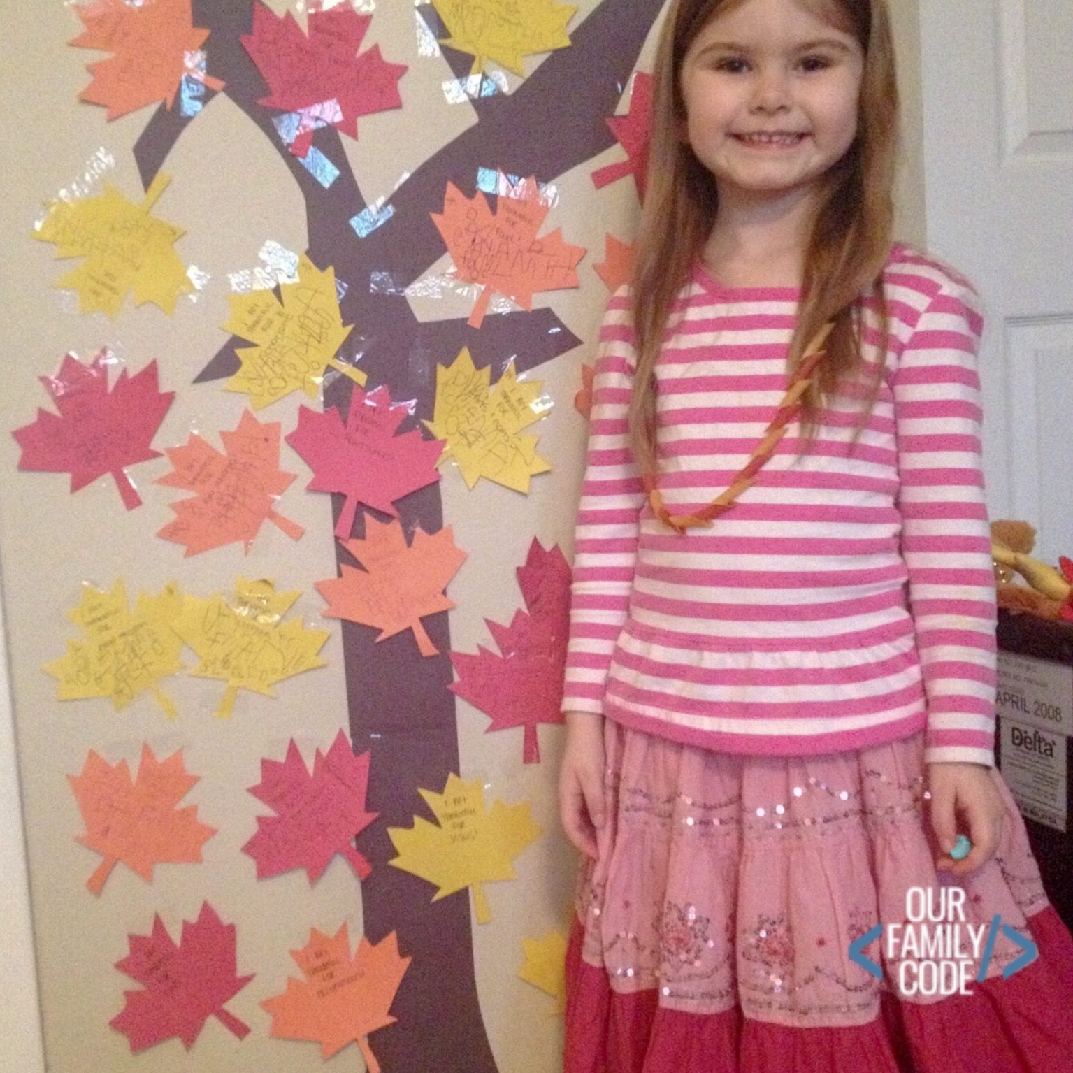 A picture of a preschooler standing next to a completed Thankful tree in the fall.