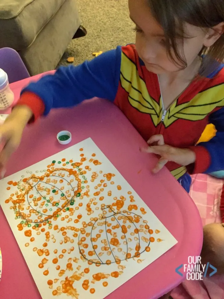 A preschooler painting a pumpkin picture with cotton swabs.