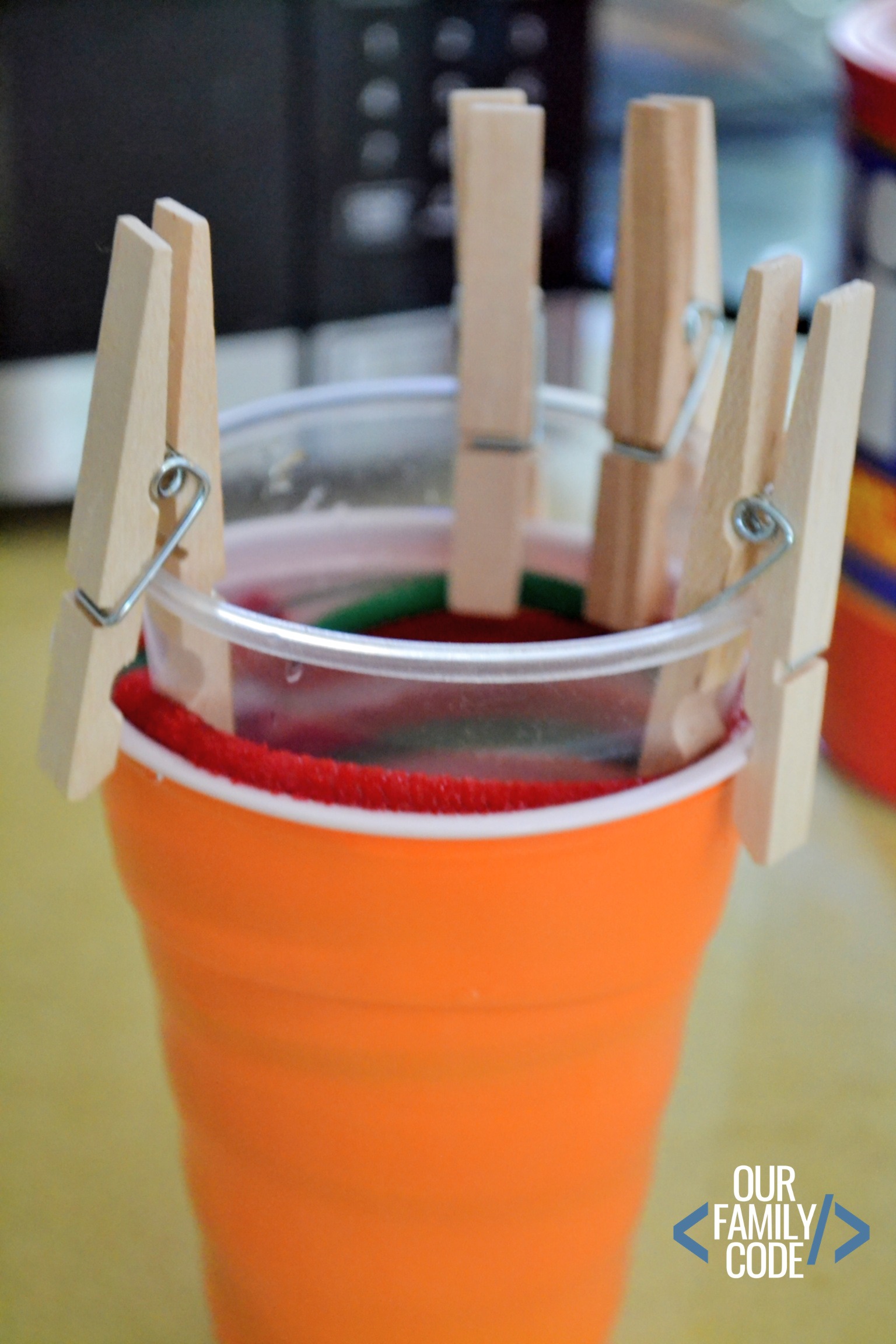 A picture of how to make an ice lantern using clips to hold a cup in place in freezer.