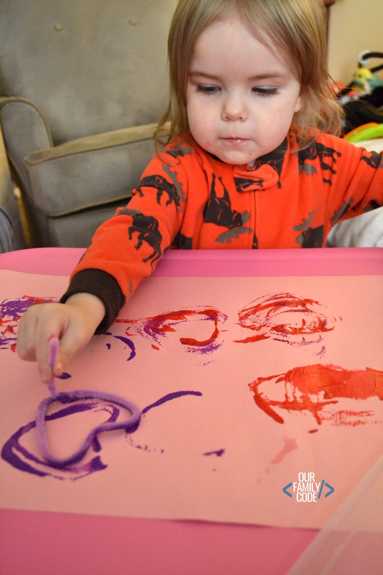A picture of a toddler stamping pipe cleaner hearts onto pink construction paper.