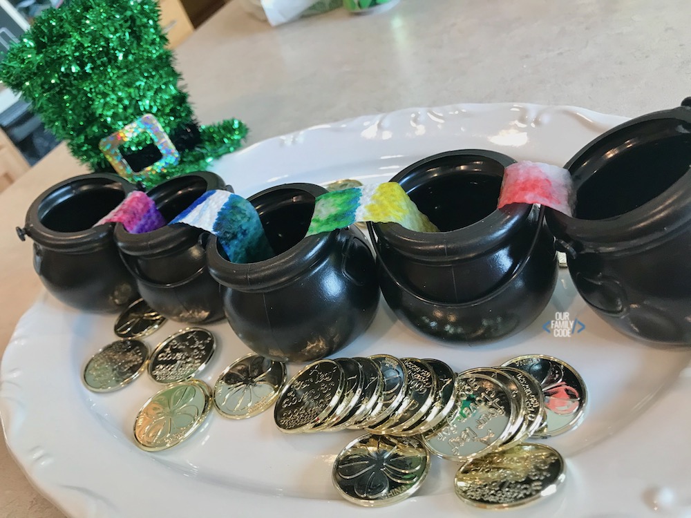 a picture of black cauldrons with rainbow paper towels between them surrounded by gold coins on white plate.