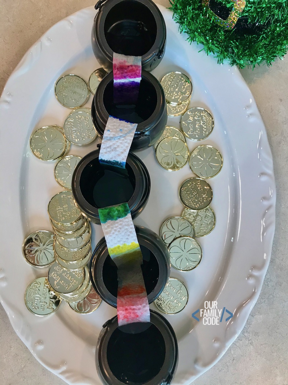 a picture from bird's eye view of rainbow paper towels in black cauldrons on white plate surrounded by gold coins.