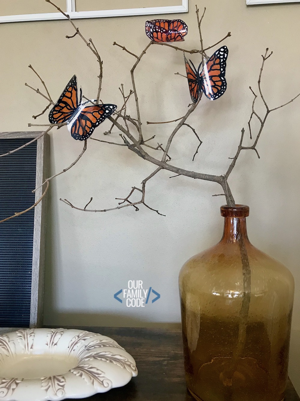 A picture of three plastic bottle butterflies displayed on a branch in an amber vase.