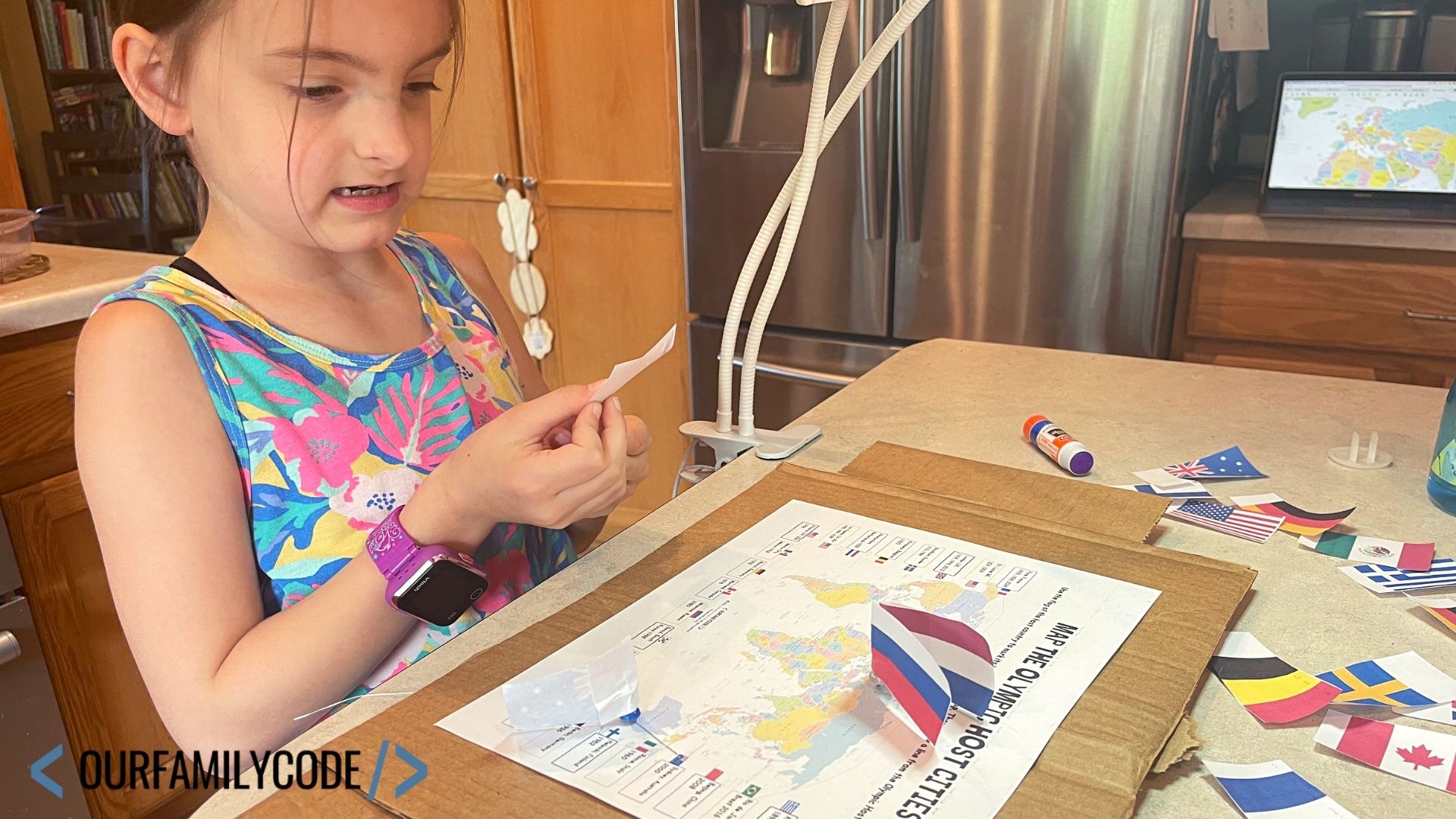 A picture of a child marking Olympic host cities on a printed map with cardboard underneath it and printed national flags made into map markers.