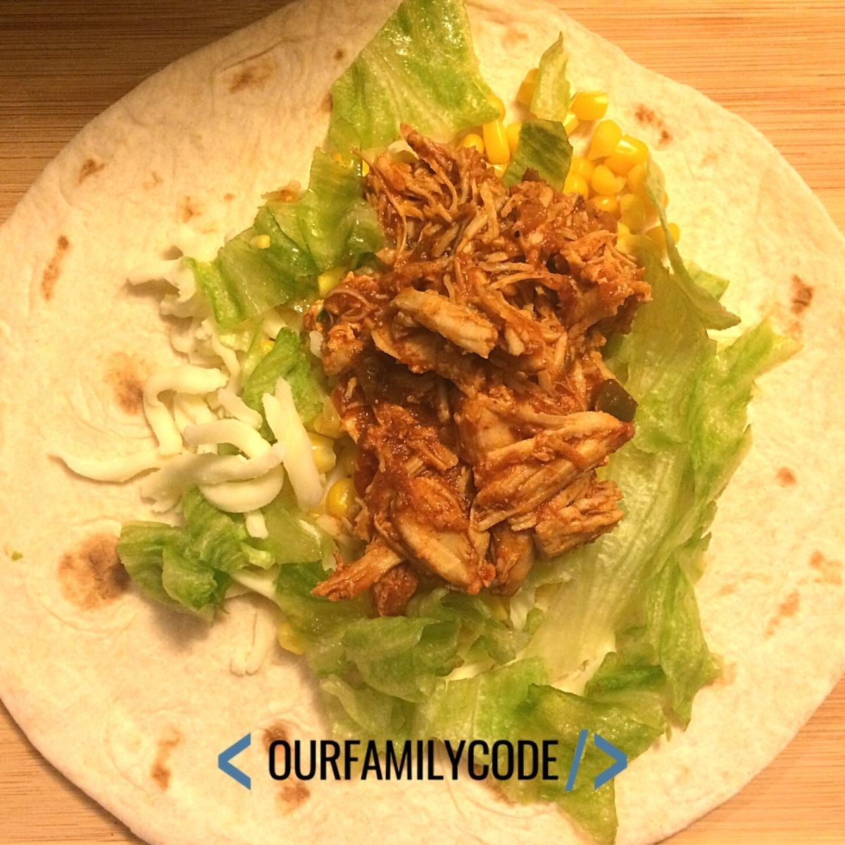 A picture of a shredded chicken taco on a soft tortilla with lettuce corn and cheese.
